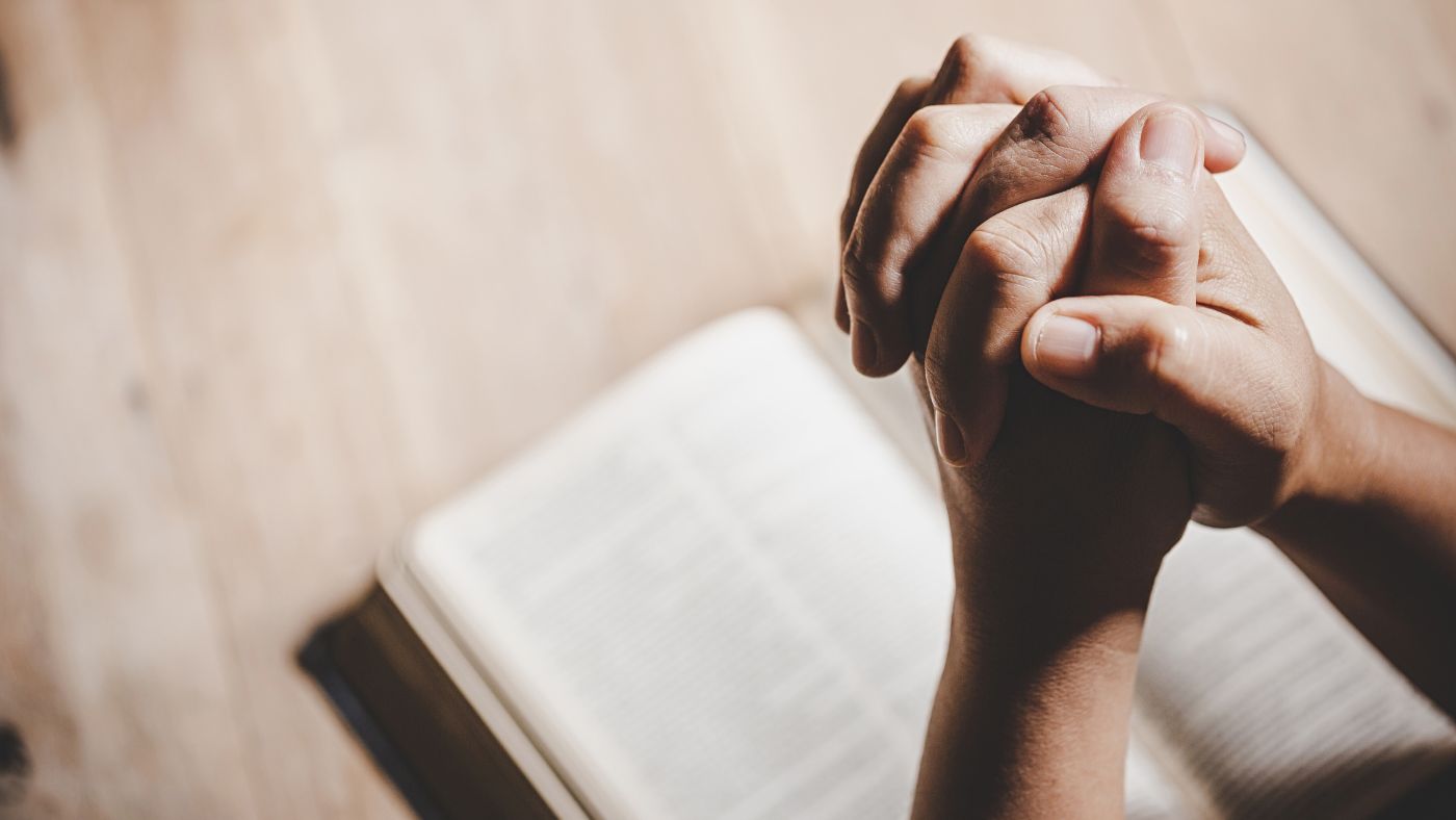 Person praying with hands closed over a Bible